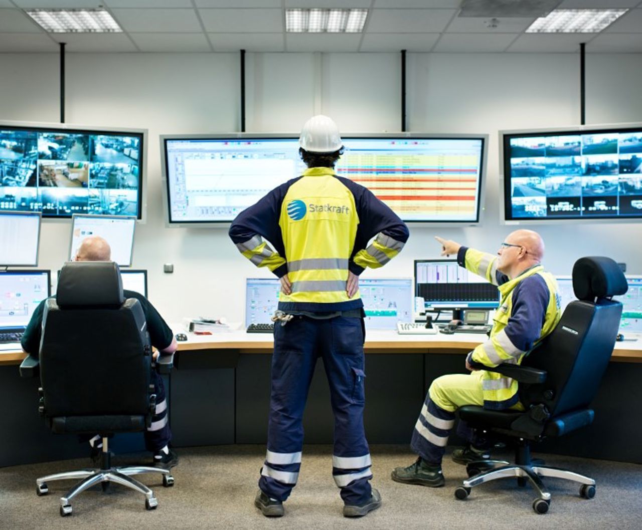 3 Statkraft Mitarbeiter in Schutzkleidung vor einer Wand mit Monitoren