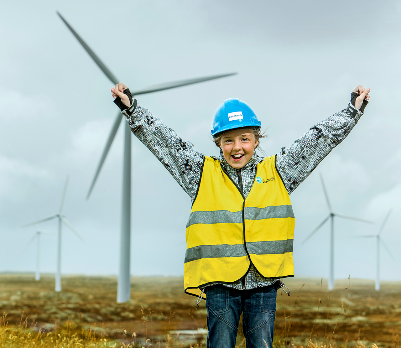 Kind in Schutzkleidung jubelt vor einem Windpark