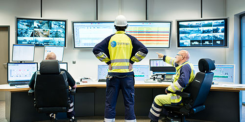 3 Kraftwerkmitarbeiter blicken auf Kontrollbildschirmen