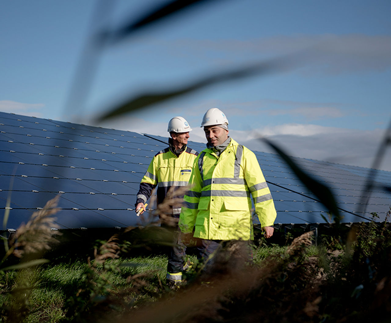 2 Mitarbeiter von Statkraft in Schutzkleidung laufen durch einen Solarpark